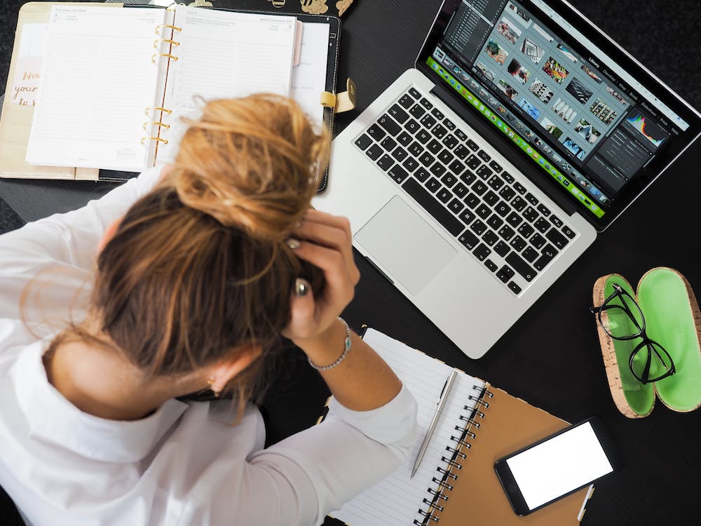 Person holding their head whilst working with laptop and notebook