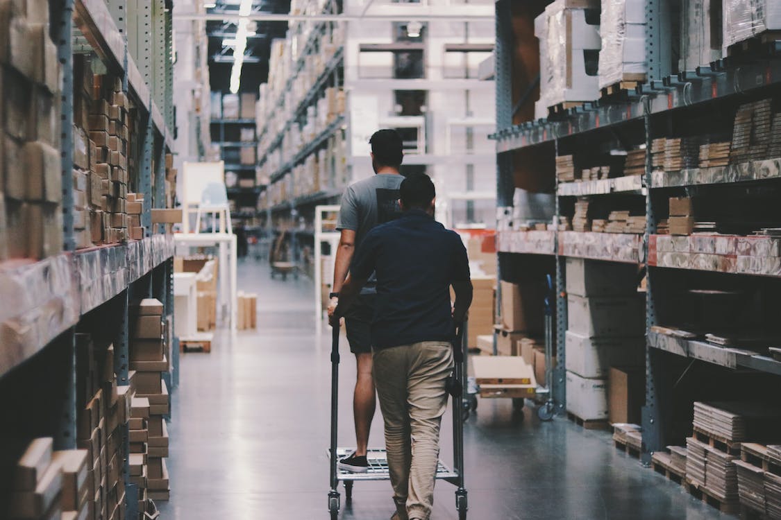 Two people walking in warehouse with stocked shelves.