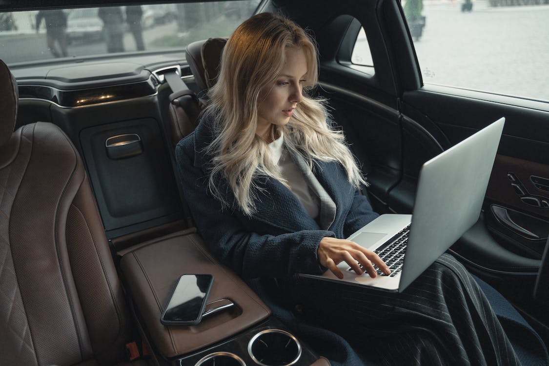 Woman working on a laptop in the back of a car.