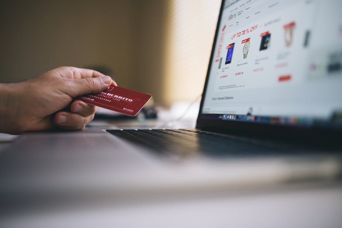 Hand holding credit card in front of screen showing an eCommerce store
