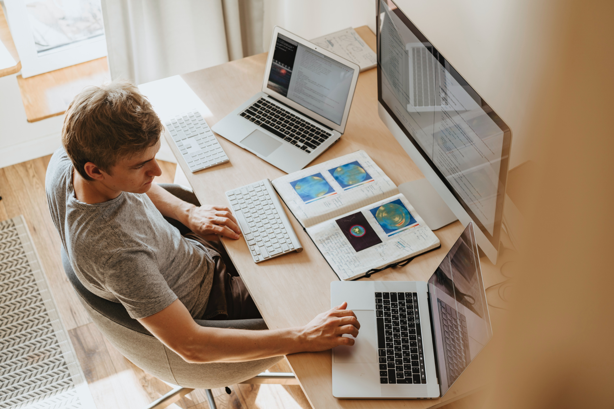 Person working at desk, with two laptops, a screen and an open book