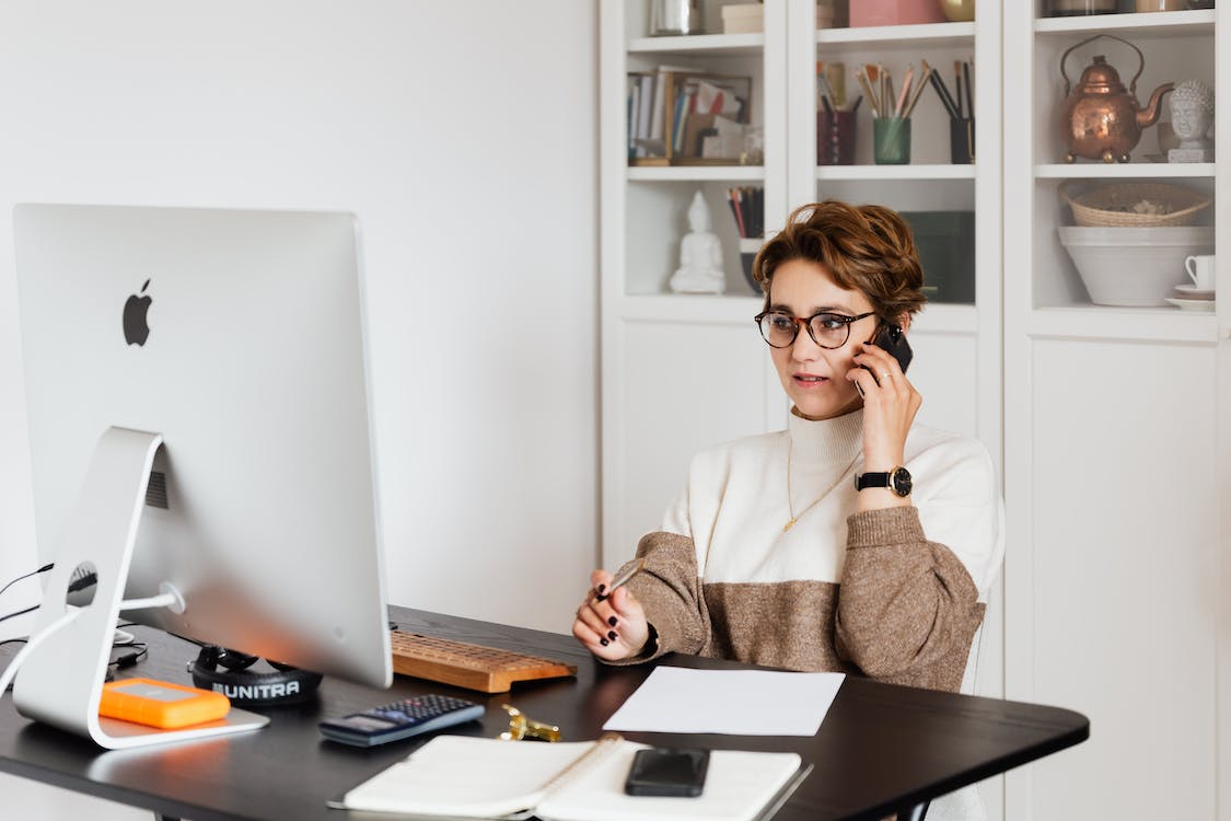 Woman wearing glasses talking on phone whilst looking at computer screen