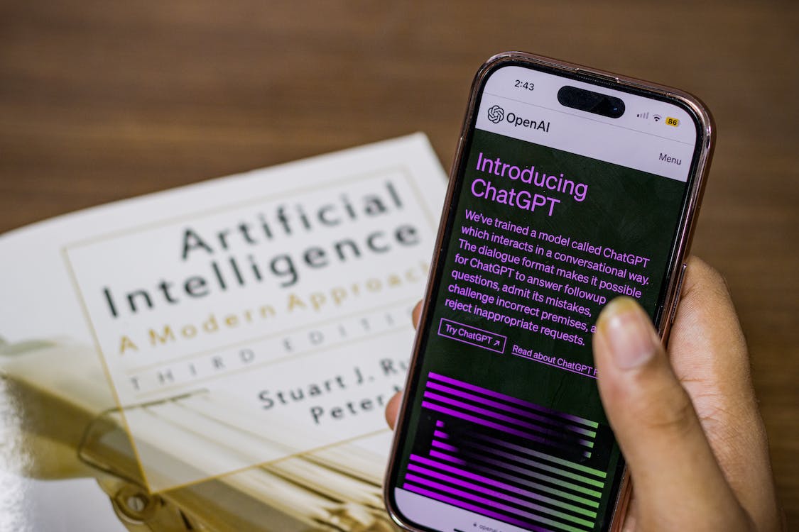 Phone showing ChatGPT page, with a book on AI in the background.