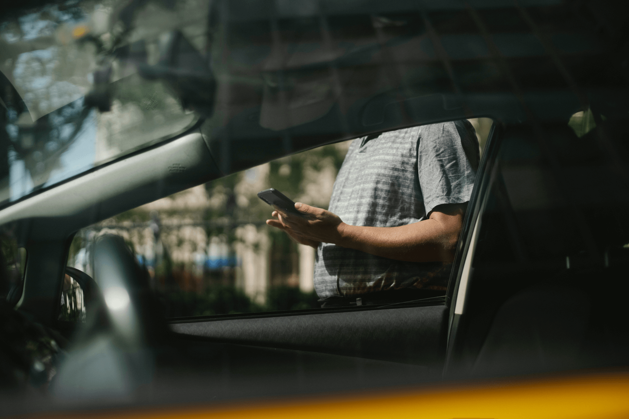 Person looking at phone, standing next to a car