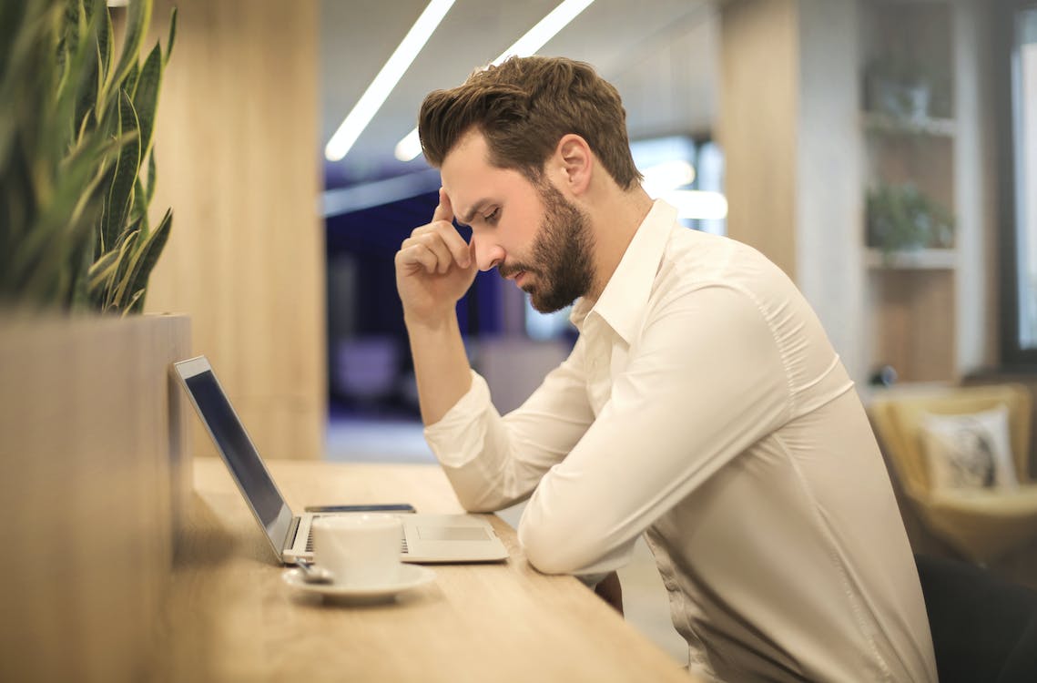 Person looking stressed, holding head whilst looking at laptop