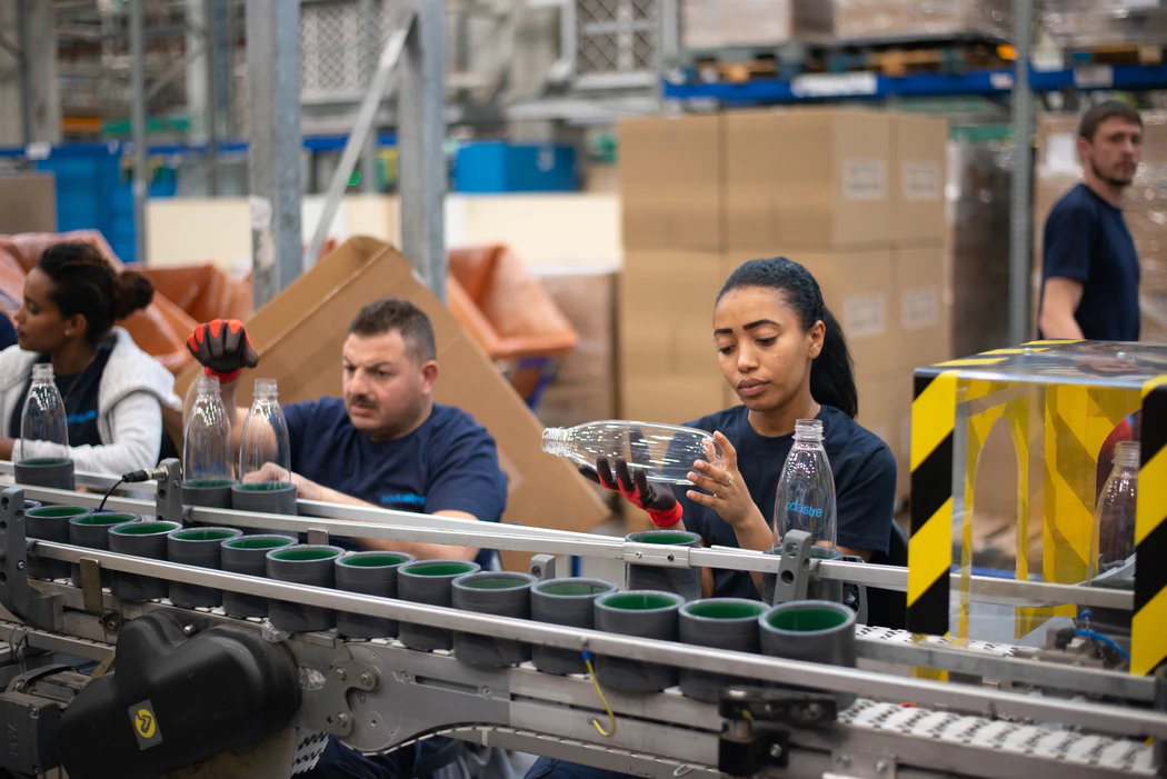 Workers in a factory inspect glass bottles before shipping them off